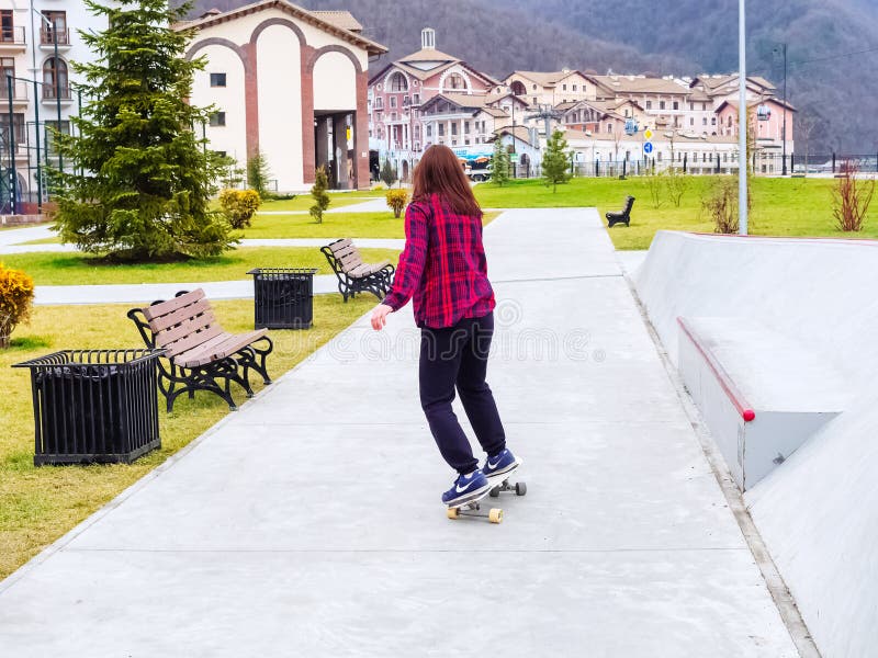 Sochi, Russia - 26 December 2019. A girl in a plaid shirt rides a skateboard on a concrete sidewalk in a resort town royalty free stock image